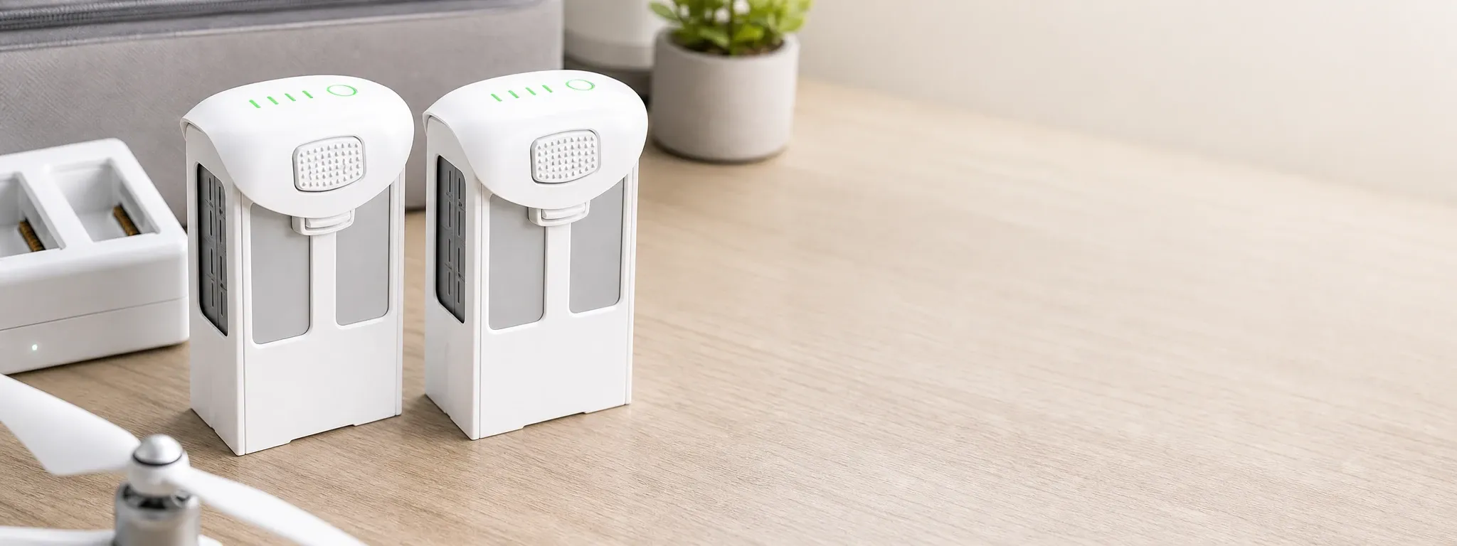 Two replacement batteries for DJI Phantom 4 series on a wooden surface, with a charging dock in the background and a small plant for context.